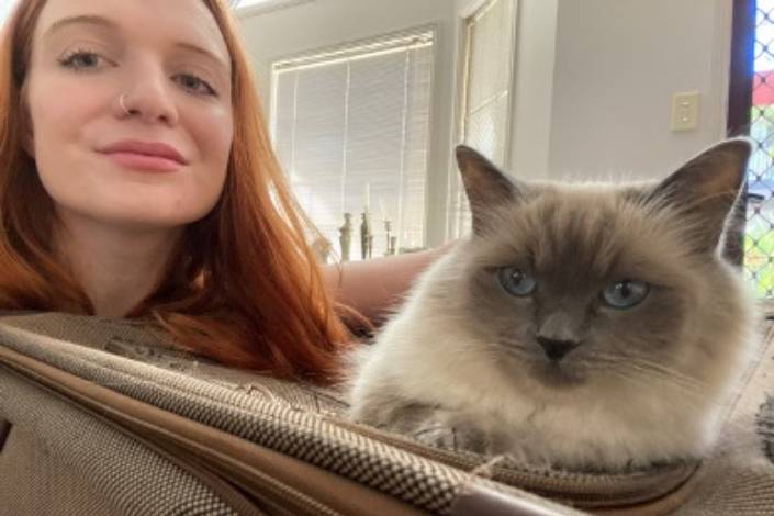 house sitter with long red hair sitting next to a white and grey fluffy cat
